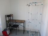 a room with a desk and clothes rack in it
