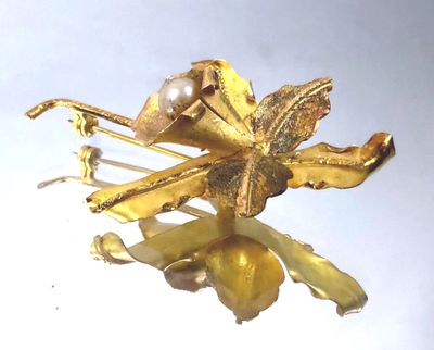a gold flower brooch with a pearl in it
