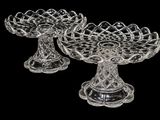 pair of clear glass footed dishes on pedestals against a black background