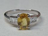 une photo d'une bague sertie d'un saphir jaune et de diamants, posée sur une surface blanche