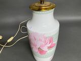 a white vase with a pink flower on it and a gold lamp