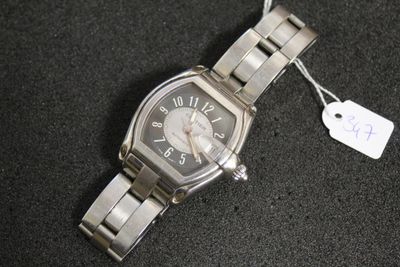 une montre en argent avec une étiquette, posée sur une surface noire
