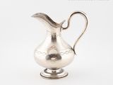 a silver pitcher sitting on a stand on a white surface