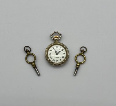 un gros plan d'une montre de poche et de deux clés posées sur une surface blanche