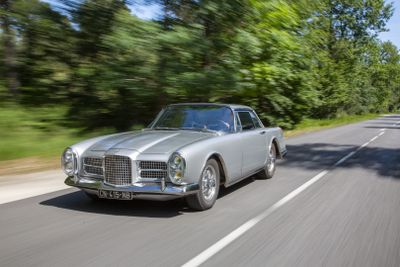 a silver car driving down the road with trees in the background