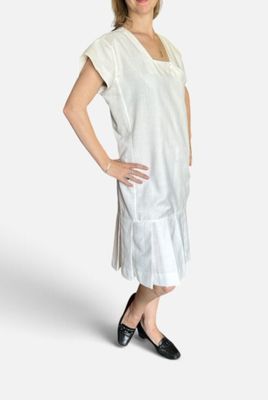 une femme enceinte en robe blanche, debout, les mains sur les hanches