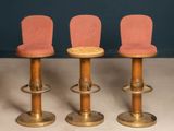 three wooden stools with pink upholstered seats sit in front of a blue wall
