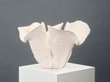 white sculpture of three flowers on a white pedestal against a gray background