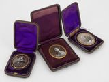 trois petites boîtes violettes sur lesquelles figurent des photos d'hommes, posées sur une surface blanche