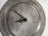 a silver clock sitting on top of a table next to a cup