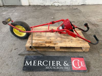 un tracteur rouge avec une roue jaune posé sur une palette à côté d'un panneau