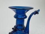 a blue glass vase with a handle on a table