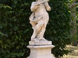 a statue of a boy holding a bird on a pedestal in a garden