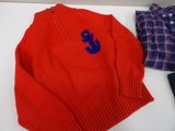 a red sweater with a blue anchor on it next to a plaid shirt