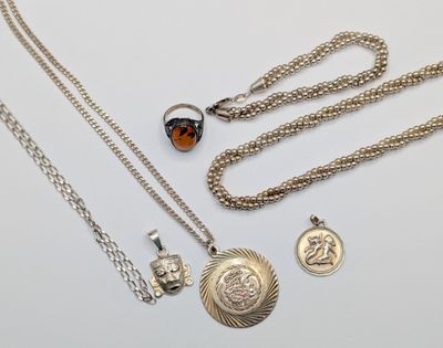 three silver necklaces and two silver charms on a white surface