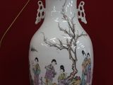 a white vase with a painting on it on a red surface