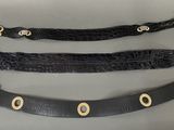 three black leather belts with gold buckles on a gray surface