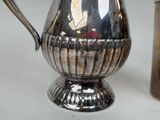 a silver pitcher next to a silver cup on a table