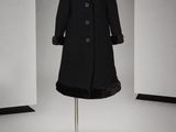 un manteau noir posé sur un pied de mannequin dans une pièce blanche