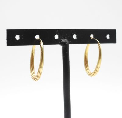 un gros plan sur une paire de boucles d'oreilles créoles en or posées sur un support noir