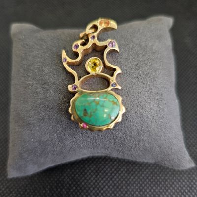 un gros plan d'un pendentif en or et en turquoise posé sur un coussin