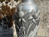 un vase en argent posé sur une table, avec un mur en pierre en arrière-plan