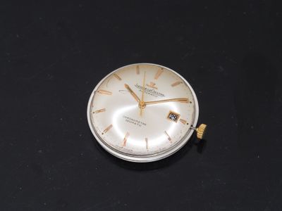 a small silver clock on a table with a black background
