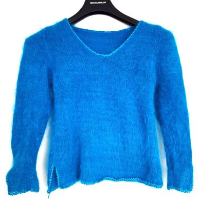 Le pull est bleu et présente des bords effilochés au niveau des manches.