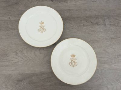deux assiettes blanches ornées de motifs dorés, posées sur une table en bois