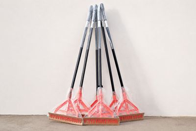 three brooms are lined up against a white wall and a broom is leaning against the wall