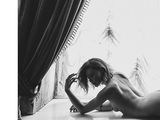black and white photograph of a naked woman laying on a window sill