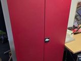 a red cabinet in the corner of a room next to a desk