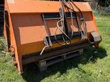une charrue orange posée au milieu d'un champ vert, à côté d'une grange