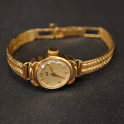 une montre en or montée sur un bracelet en or, posée sur une surface noire