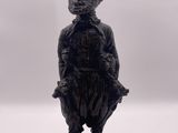 statue noire représentant un homme coiffé d'un chapeau, sur fond blanc