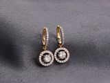 a pair of gold and diamond earrings on a gray fabric