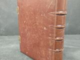 an old brown book sitting on top of a table next to a gray wall