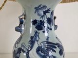 a blue and white vase on a table with a lamp on it