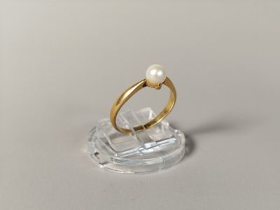 a gold ring with a pearl in it on a clear stand