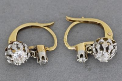 deux paires de boucles d'oreilles en or et diamants posées sur une surface grise