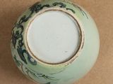 a green and white vase sitting on a brown surface