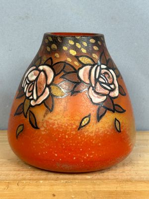 un vase orange orné de fleurs peintes, posé sur une table