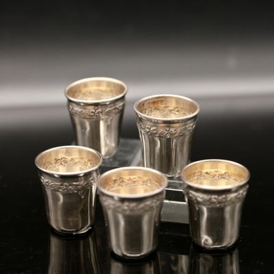 four silver shot glasses sitting on top of a tray on a table