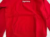 a red supreme hoodie sitting on top of a bed
