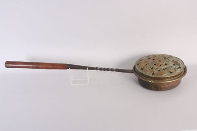 une vieille casserole en laiton avec une poignée en bois, posée sur une surface blanche