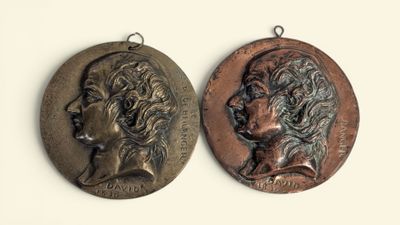 two bronze medallions of a woman and a man on a white background