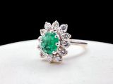 un gros plan d'une bague sertie d'une émeraude verte et de diamants, posée sur une assiette blanche