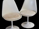 pair of white tulip chairs with beige cushions on a black background
