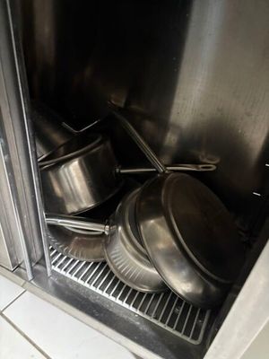 Des casseroles et poêles en acier inoxydable sont empilées sur une étagère dans une cuisine