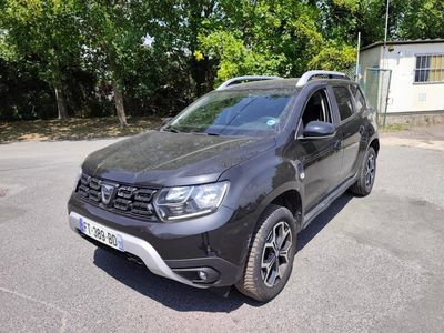 a grey dacia parked in a parking lot with trees in the background